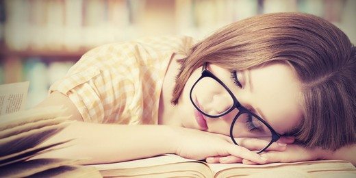 tired student girl with glasses sleeping on books in library